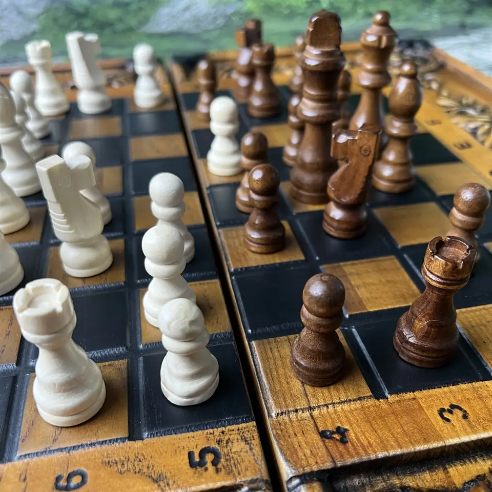 Handcrafted wooden chess pieces placed on a wooden chess board, light and dark figures close-up