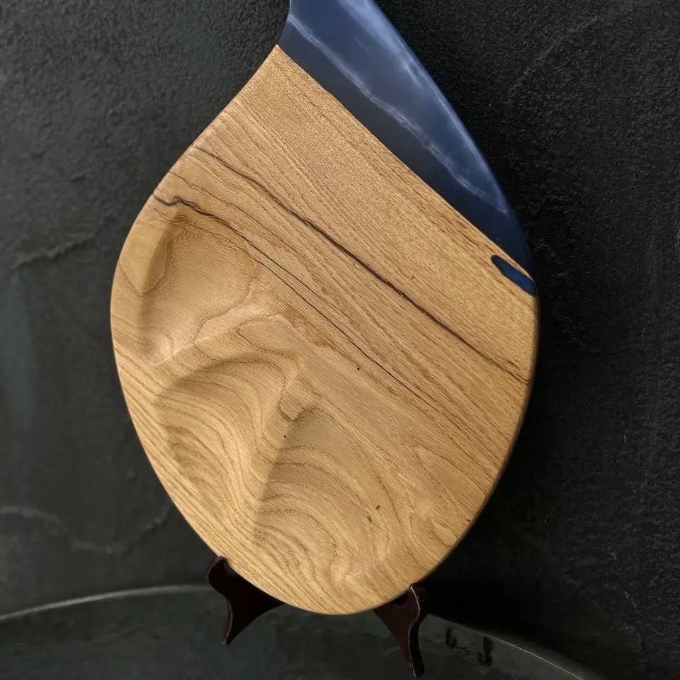 Handmade wooden cheese board with deep blue epoxy resin handle on a dark background