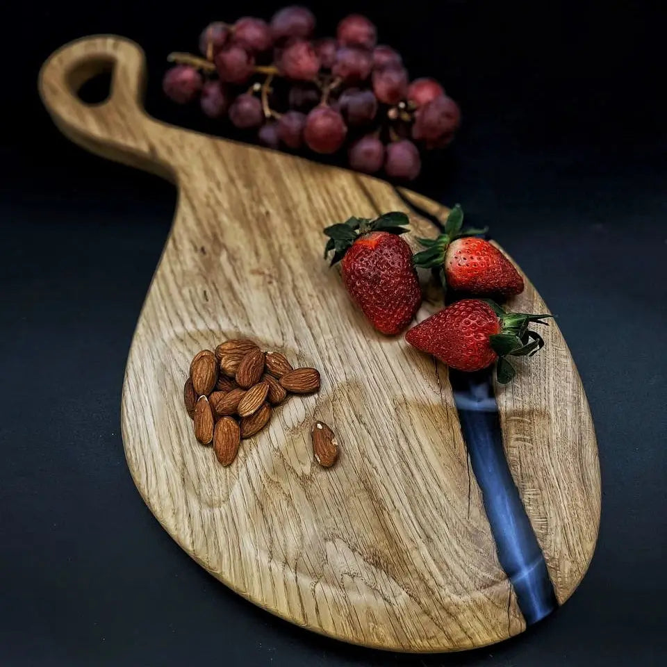 Wooden cutting board with blue epoxy resin displayed with cheese and fruit.