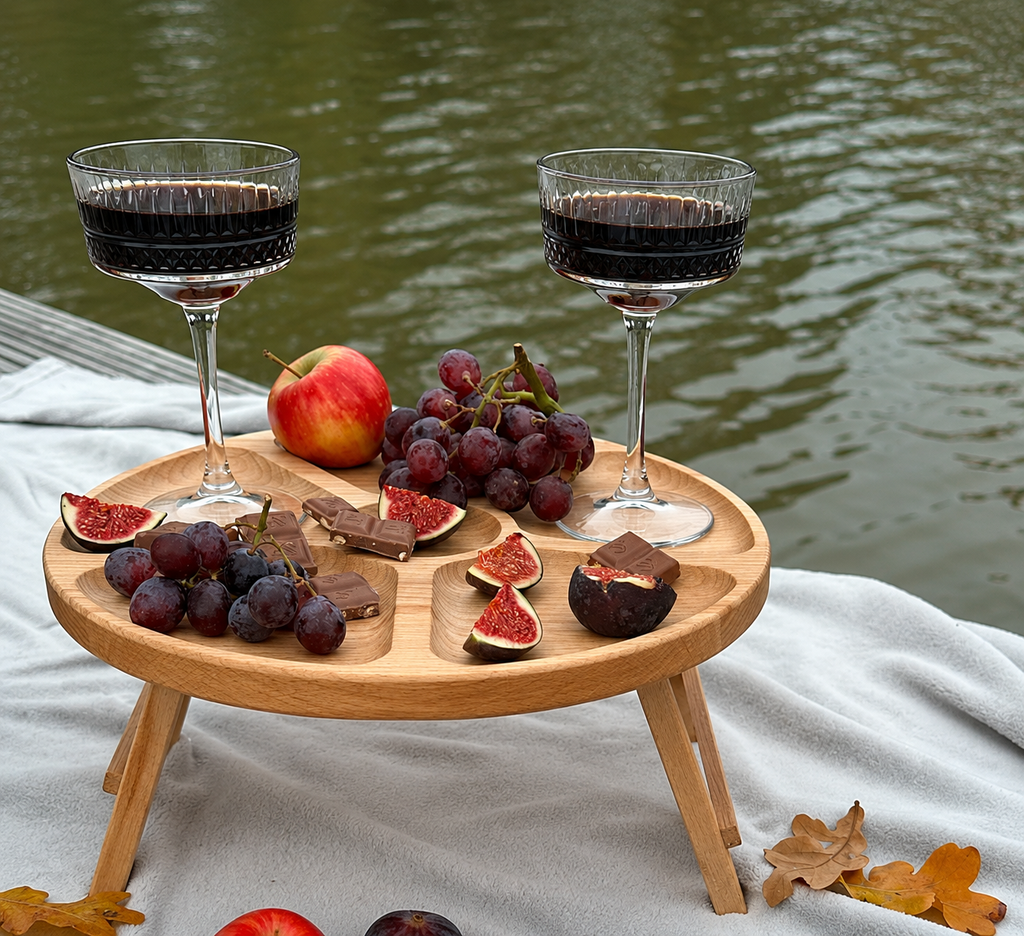 Round wooden serving table with legs displaying fruits, grapes and snacks outdoors