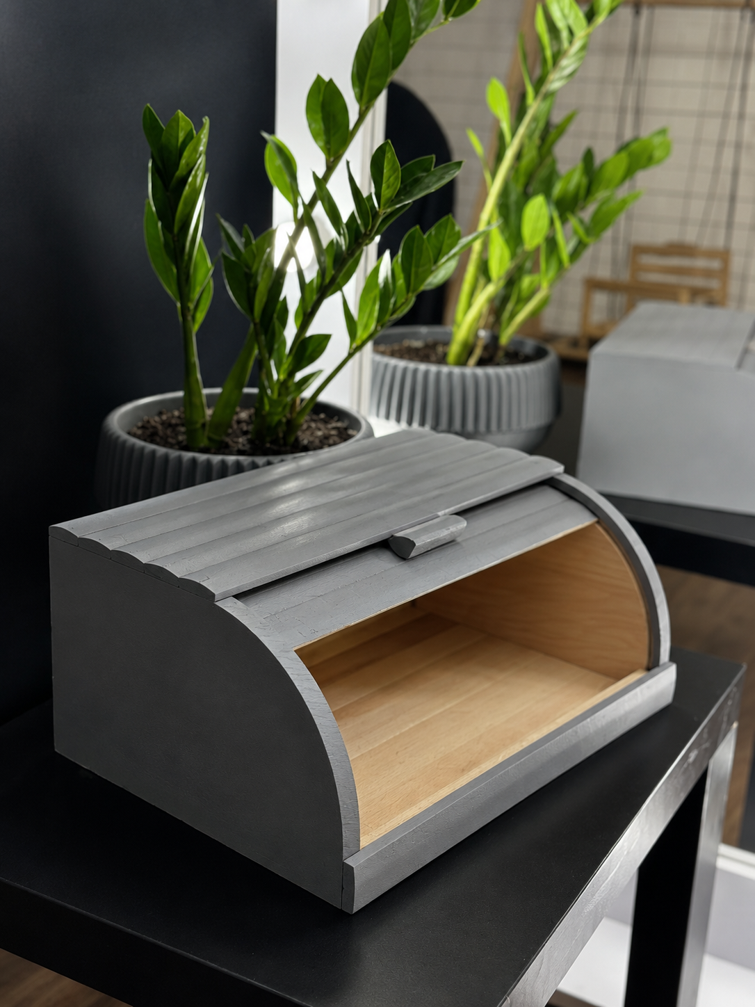 Gray wooden roll-top bread box on kitchen countertop near green plant