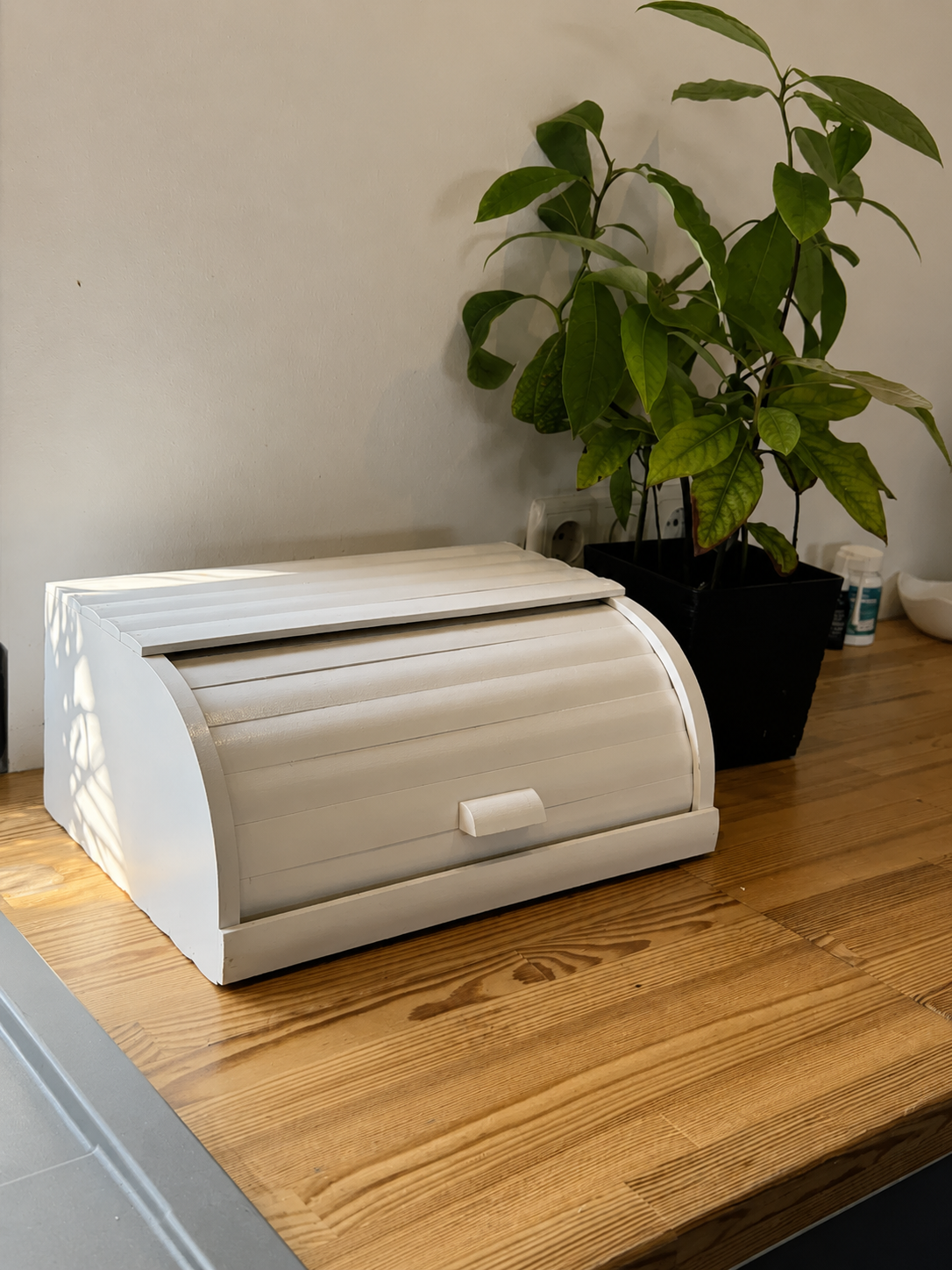 White wooden roll-top bread box on kitchen countertop