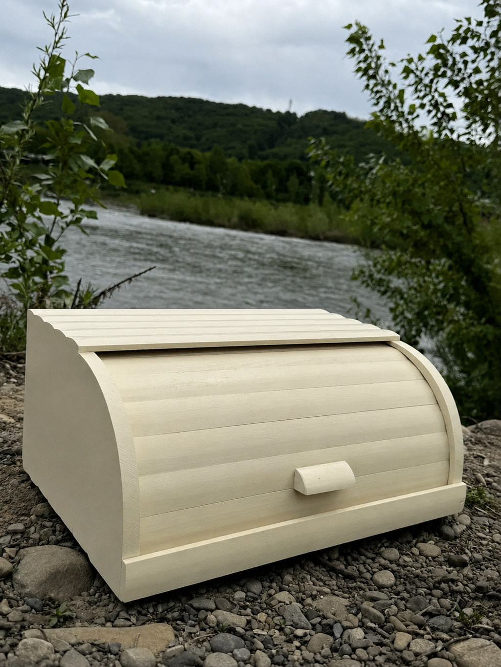 Natural beech wood bread box with roll-top lid outdoors near a river