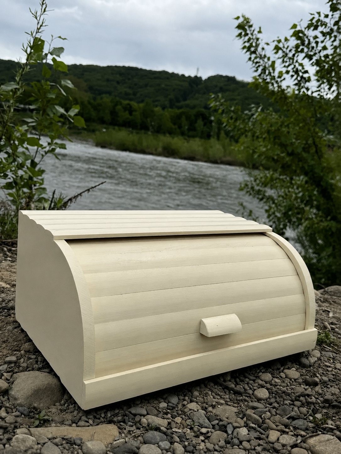 Natural beech wood bread box with roll-top lid outdoors near a river