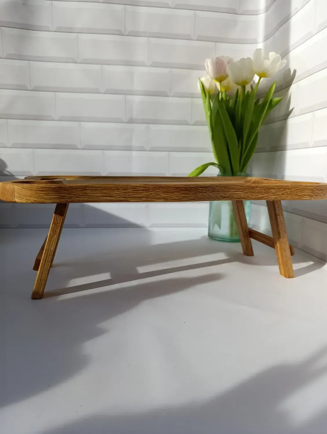 Side view of a low wooden lap desk with unique wave pattern and sturdy foldable legs.