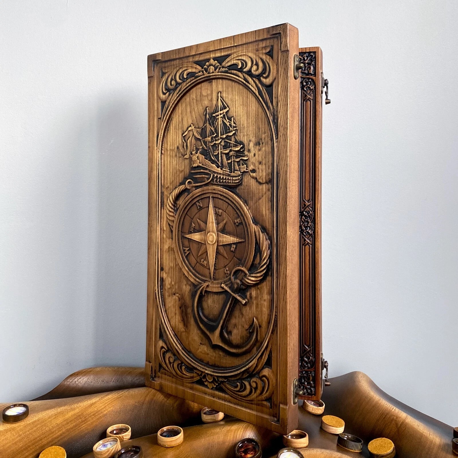 Vertical view of a carved nautical backgammon board with ship, anchor, and compass motifs.
