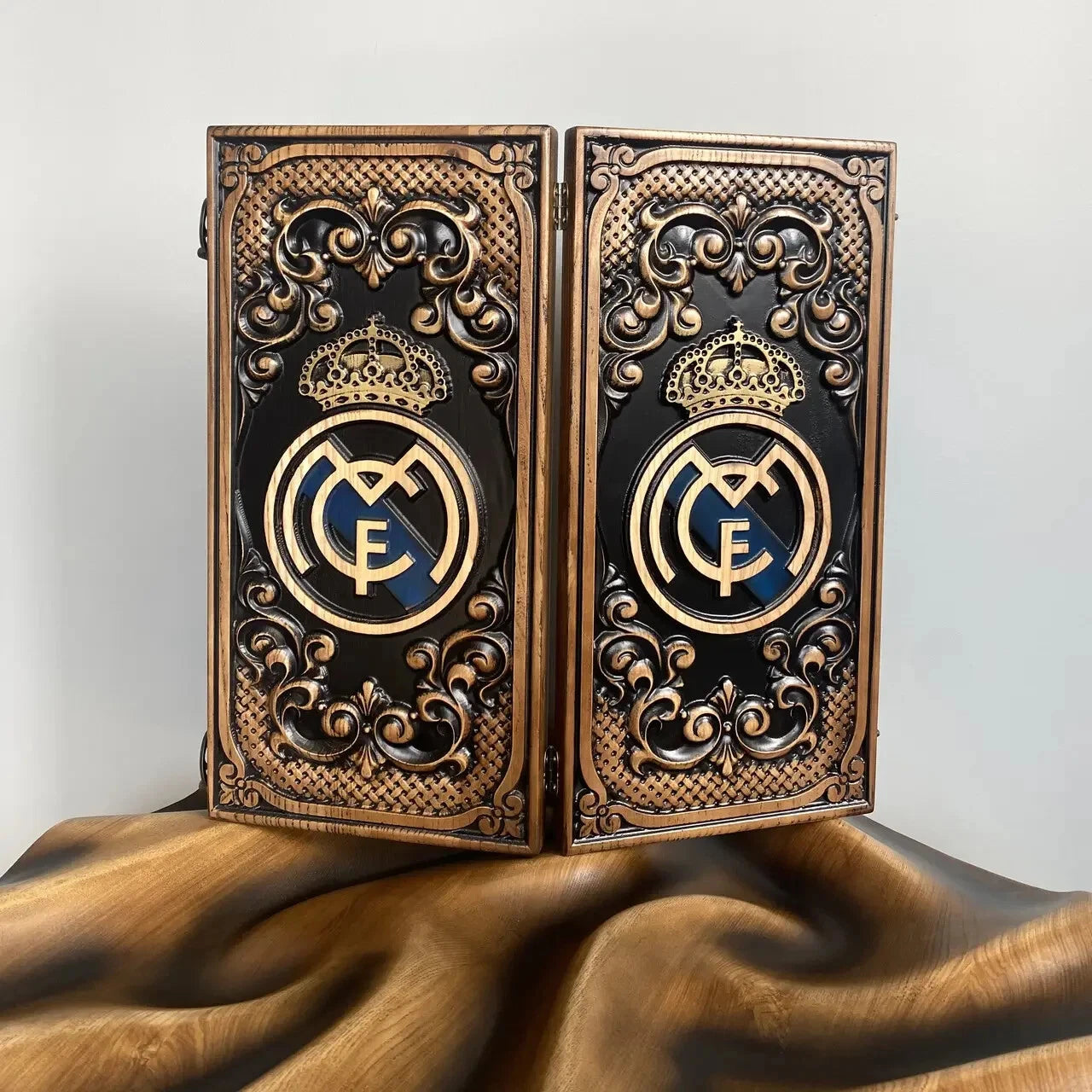 Handcrafted wooden backgammon board with ornate carvings and a gold royal-style emblem on a black background.