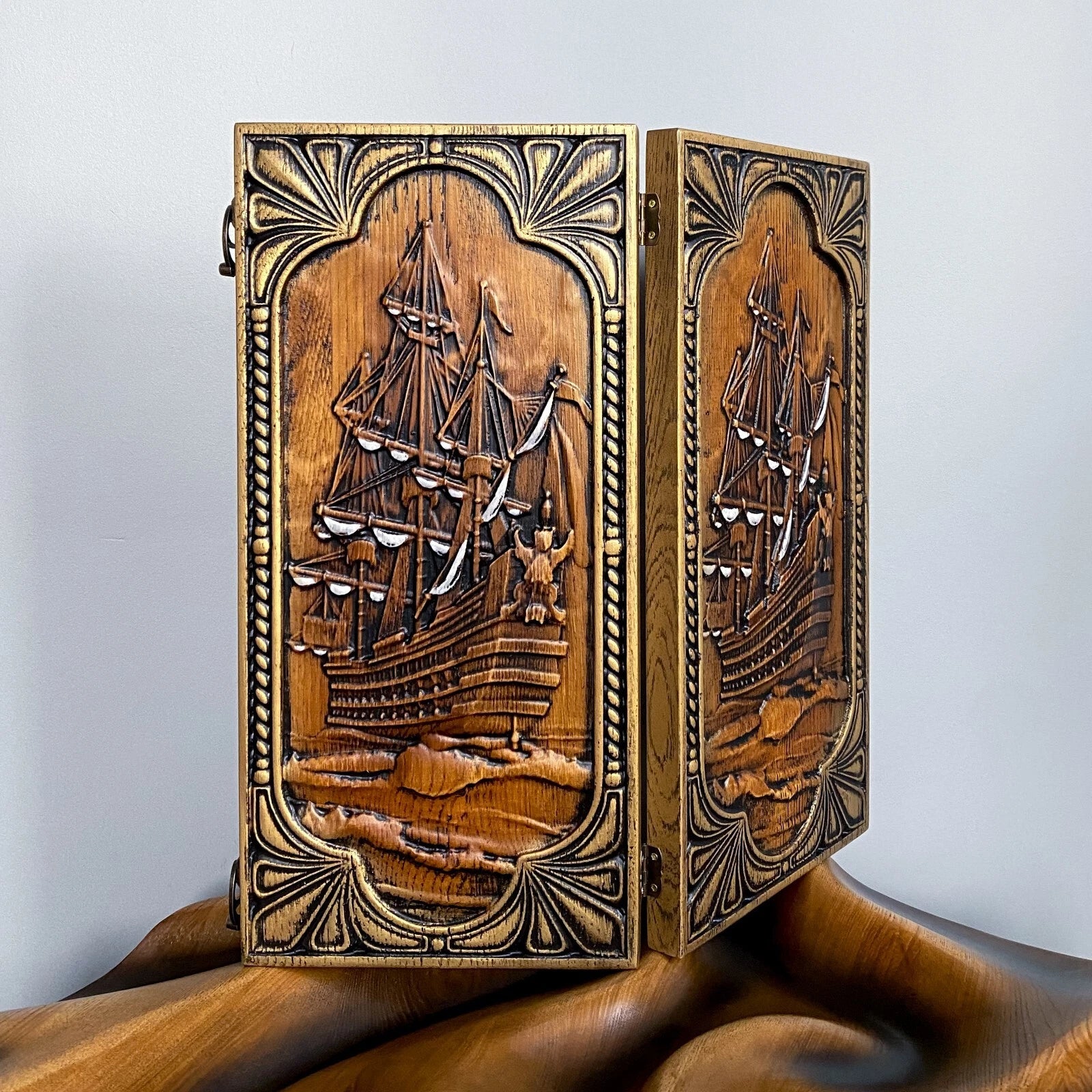 Hand-carved wooden backgammon board with a detailed sailing ship design, standing upright on a wooden surface.