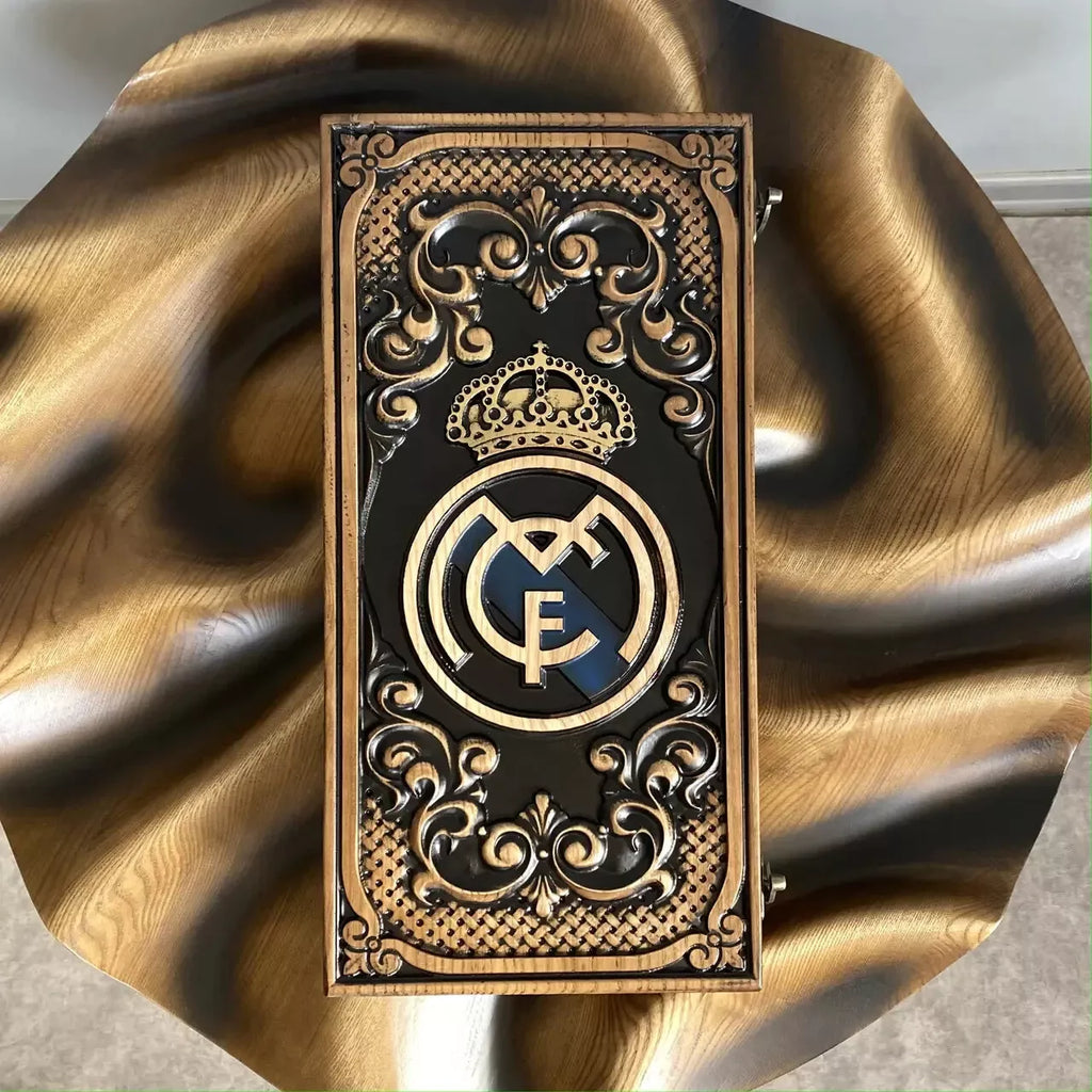 Top view of a handcrafted backgammon board with detailed carving and a gold crest centerpiece.