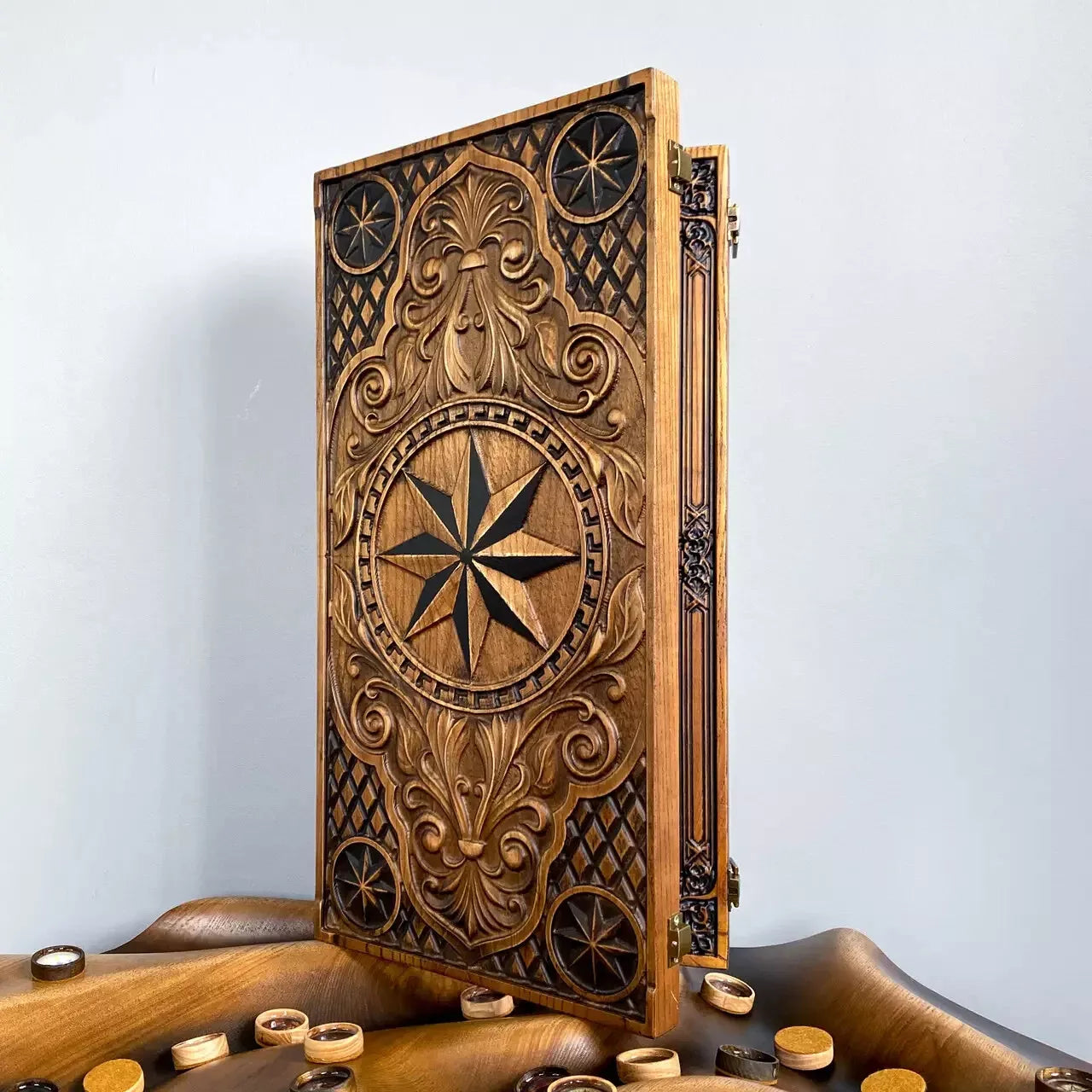 Carved wooden backgammon board with ornate compass and floral motifs standing upright on a wooden surface.