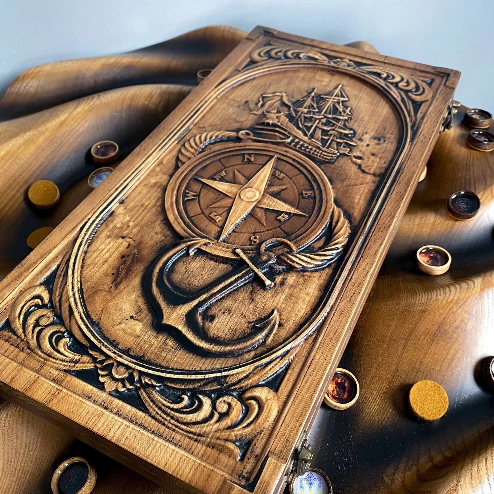 Closed wooden backgammon board with detailed carvings of a ship, compass, and anchor in a nautical theme.