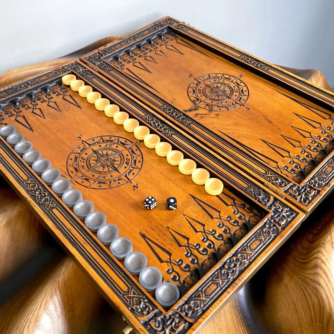 Handmade wooden backgammon board opened flat, decorated with compass engravings, complete with playing chips and dice.