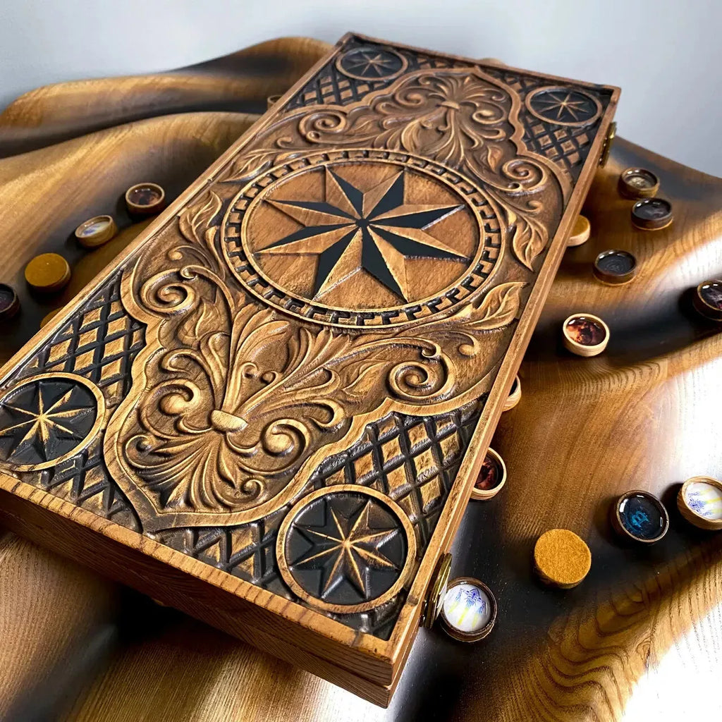 Handmade ash wood backgammon set with detailed compass carving placed on fabric with chips arranged around.