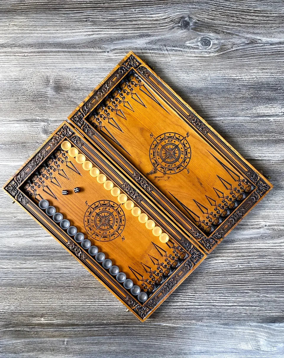 Open wooden backgammon board with compass engraving, chips, and dice arranged for gameplay.