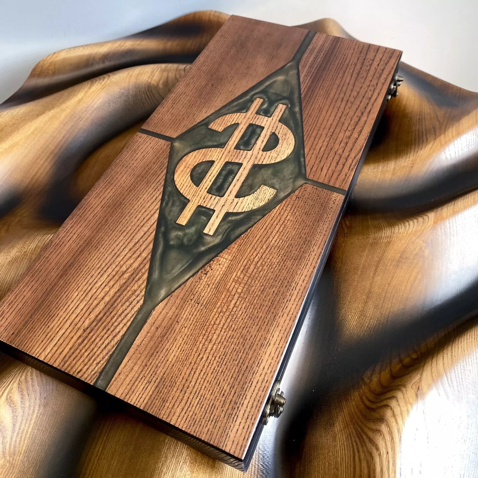 Closed wooden backgammon board with carved dollar symbol and green resin diamond, photographed from an angled top view.