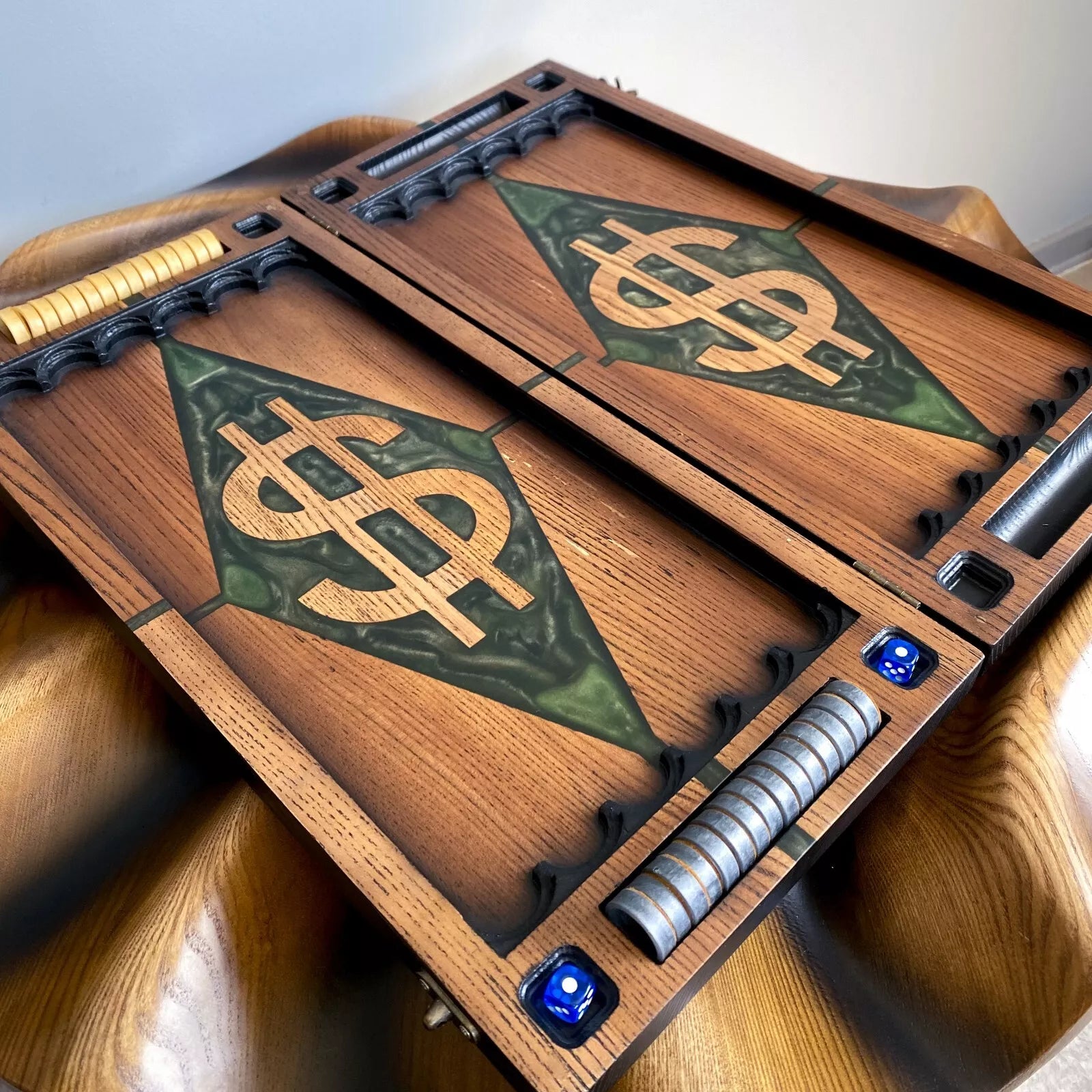 Open wooden backgammon board with green resin diamond and carved dollar symbol, complete with metal checkers and blue dice.