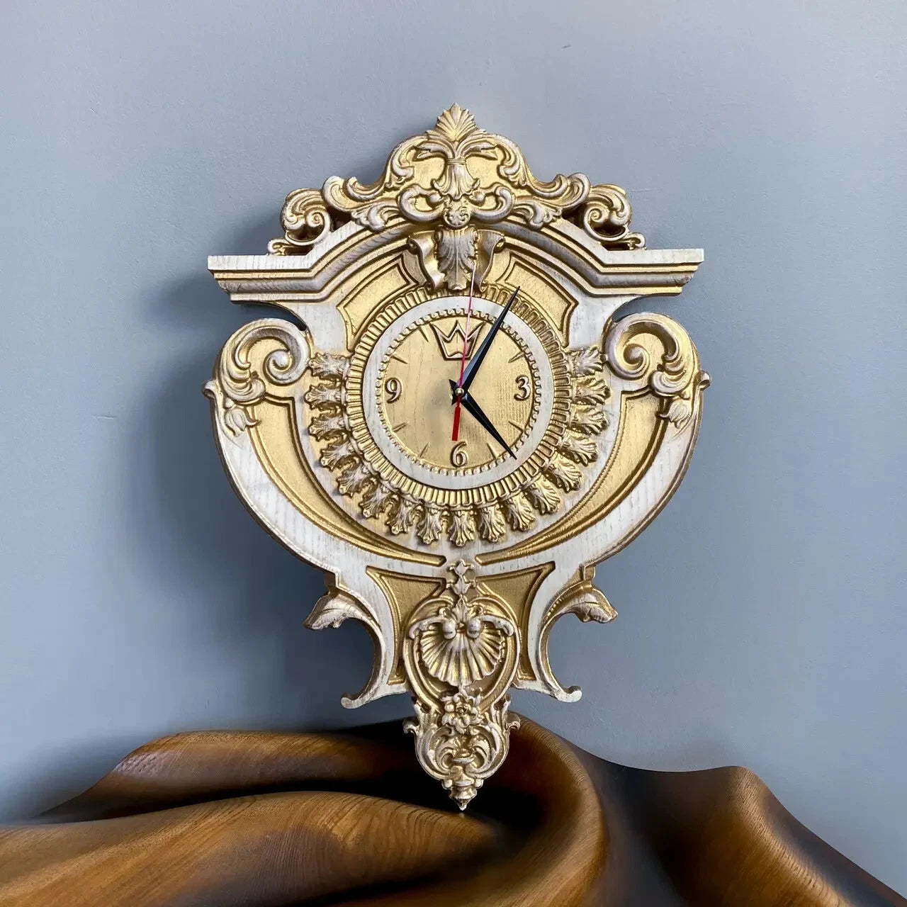 Handcrafted baroque wall clock in white and gold finish placed on wooden background, luxury decorative home clock